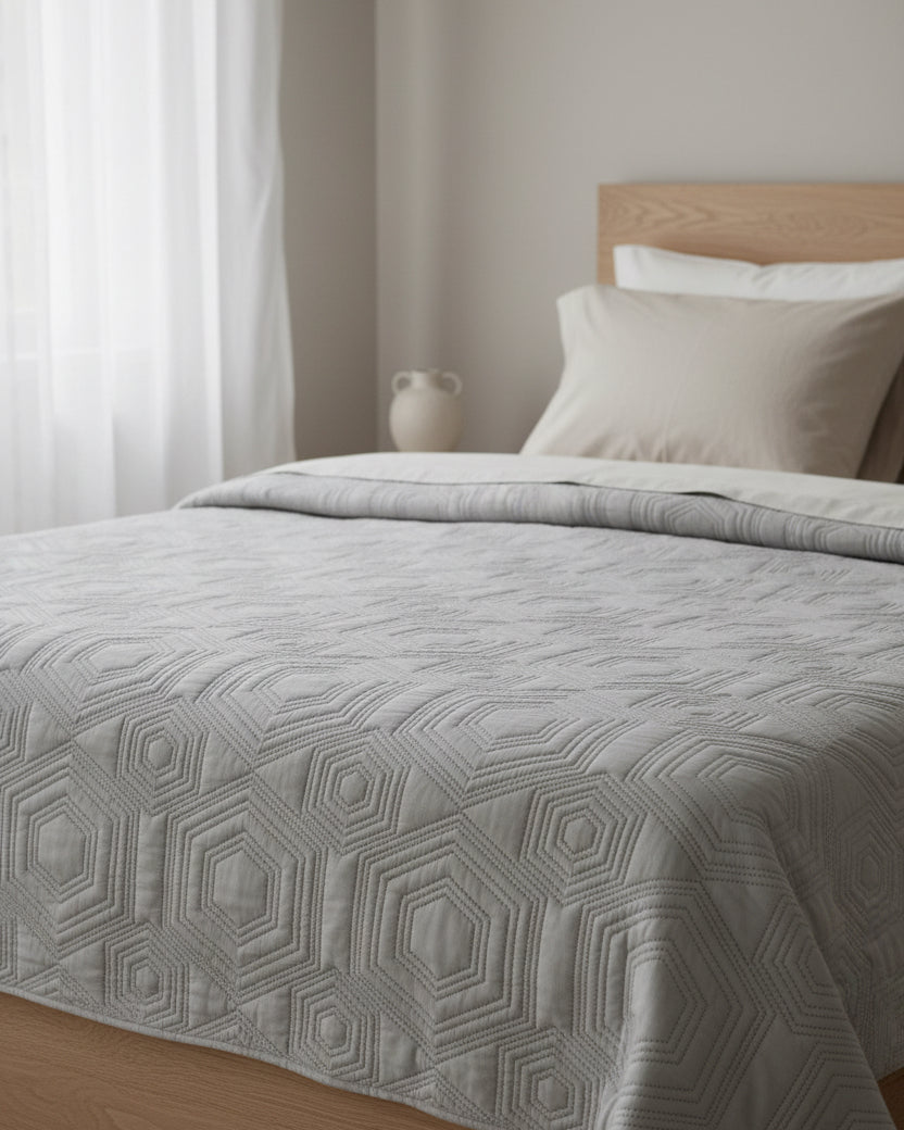 Malini Dorchester Grey geometric quilted bedspread on a double bed, showcasing soft furnishings with modern geometric pattern.