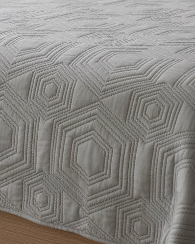 Malini Dorchester Grey Geometric Quilted Bedspread on a bed, showcasing soft furnishings with a modern grey geometric pattern.