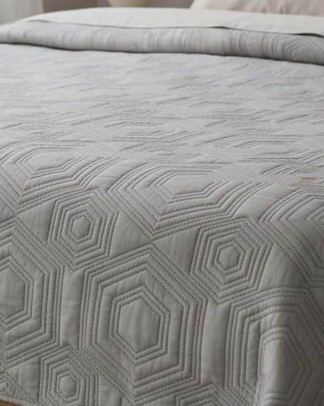 Malini Dorchester Grey Geometric Quilted Bedspread on a double bed, showcasing soft furnishings with a modern geometric pattern.