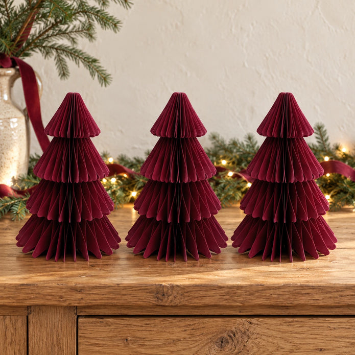 Three matching 25cm burgundy paper Christmas trees on an oak sideboard with festive greenery.