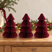 Three matching 25cm burgundy paper Christmas trees on an oak sideboard with festive greenery.