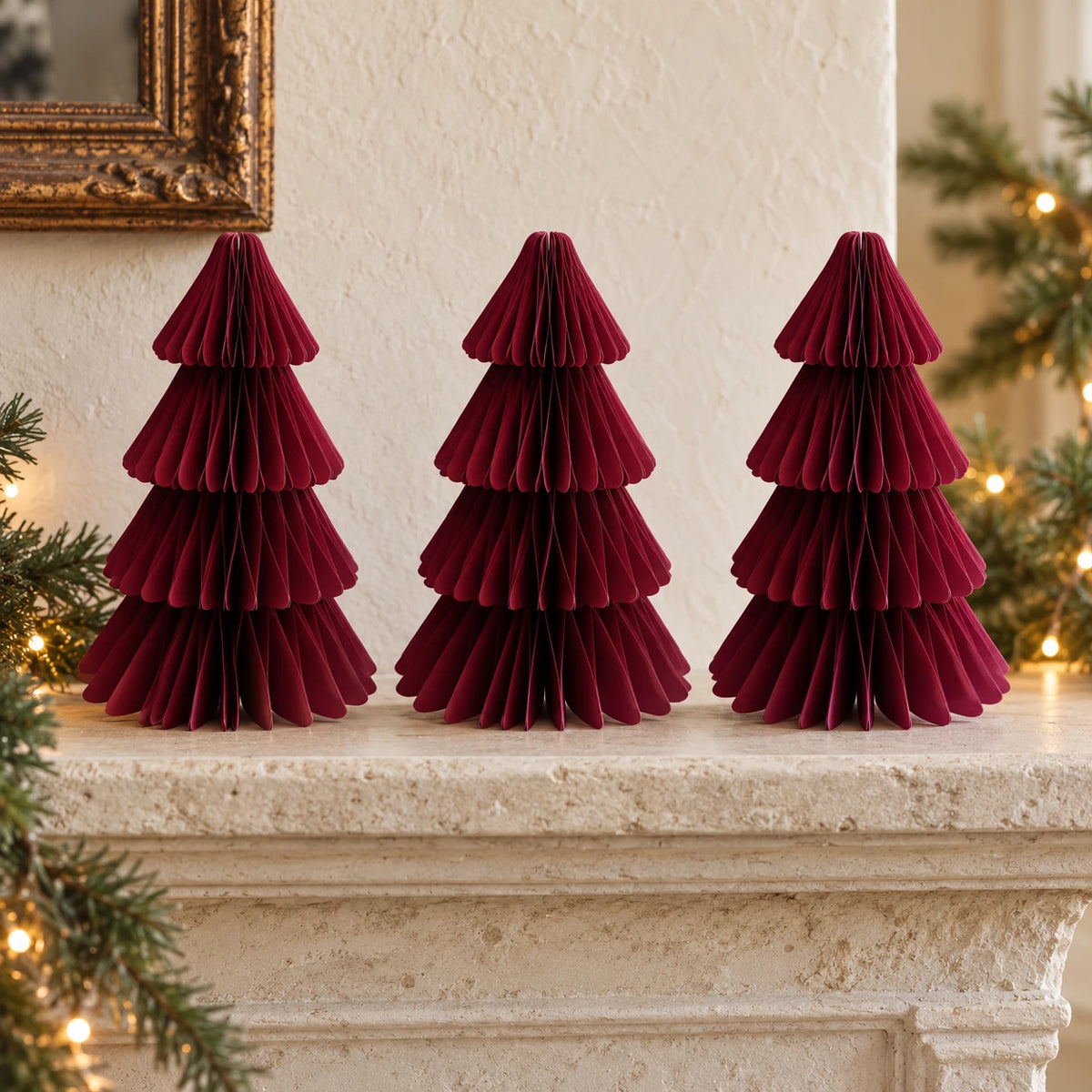 Three equal-sized burgundy paper Christmas trees side by side on a stone mantel.