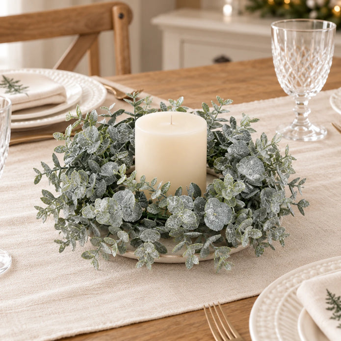Frosted eucalyptus candle wreath with an unlit ivory candle on a neutral Christmas dining table; accessories not included.