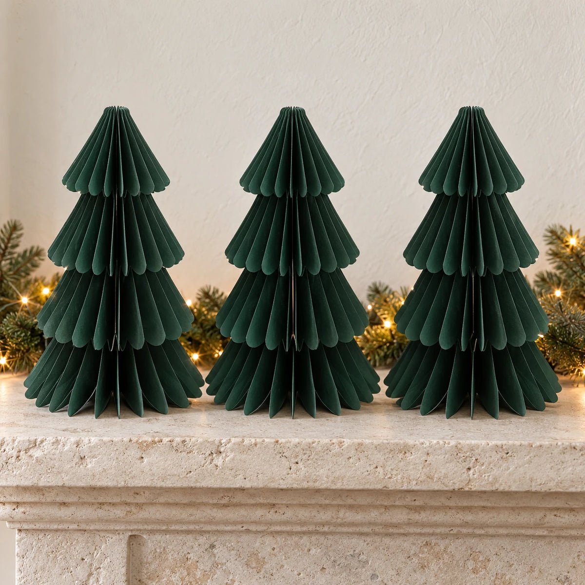 Three equal-sized green paper Christmas trees side by side on a stone mantel.
