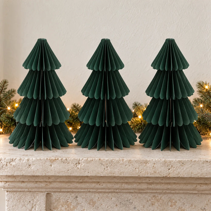 Three equal-sized green paper Christmas trees side by side on a stone mantel.