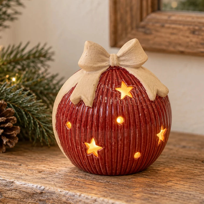 Medium red ceramic LED bauble with cream bow glowing on a light country-style console