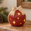 Medium red ceramic LED bauble with cream bow glowing on a light country-style console