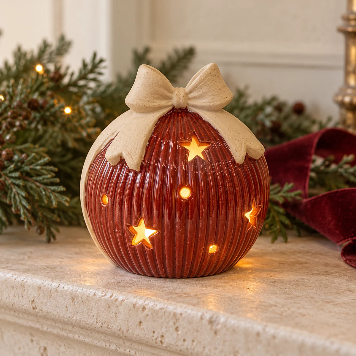 Red ceramic light-up bauble with bow displayed on a pale Christmas mantel