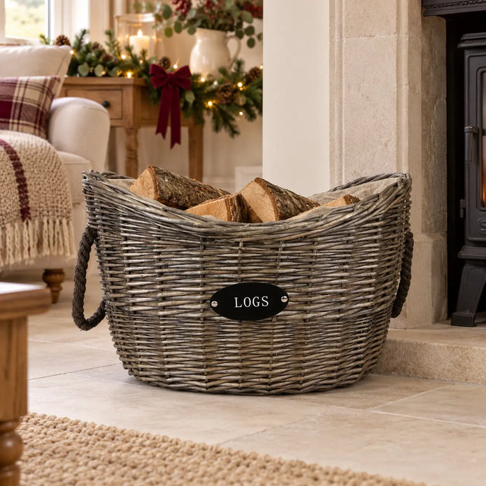 Meon oval log basket filled with logs beside a stone fireplace