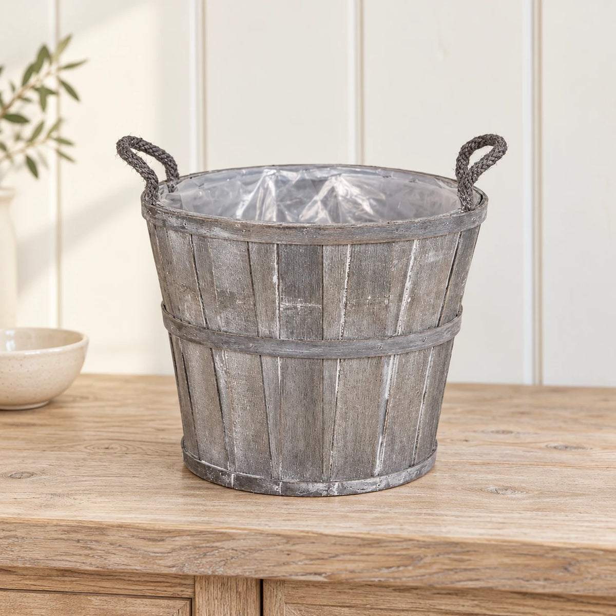 Empty medium Meon planter basket on a pale oak console with its clear liner visible