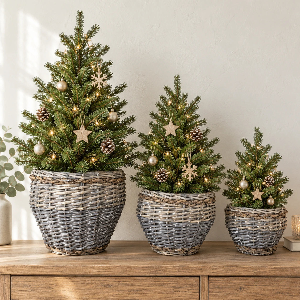 Three Meon planter baskets holding miniature decorated Christmas trees on a wooden console