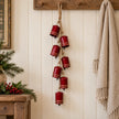 Seven glossy red cowbells on a rope garland hanging beside a Christmas display