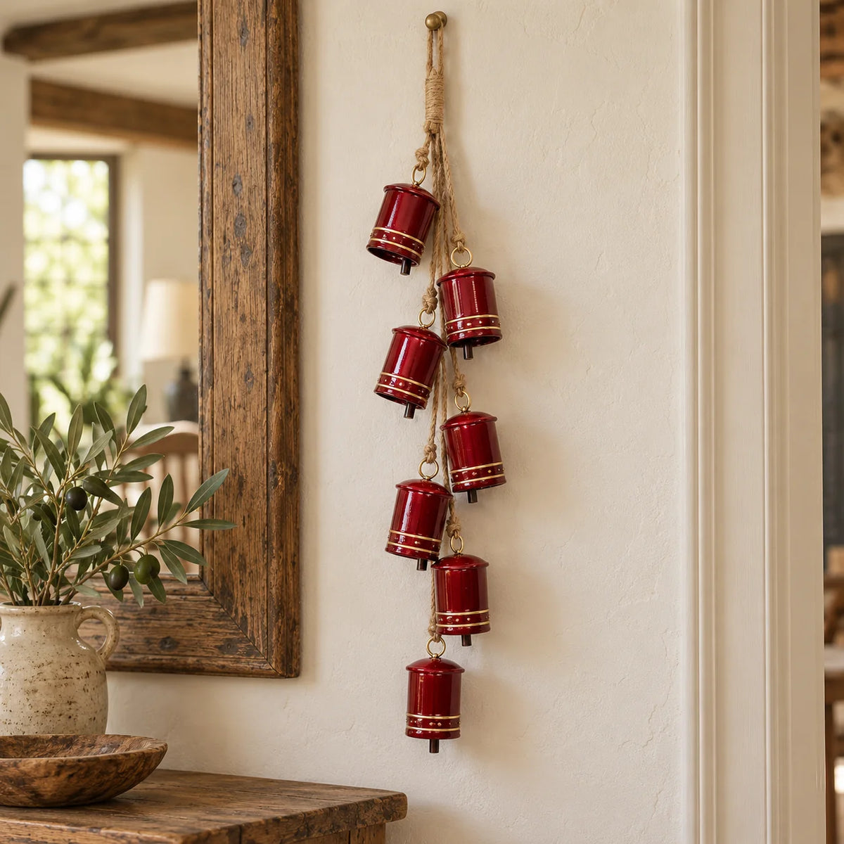 Glossy red seven-cowbell garland hanging beside a mirror and greenery