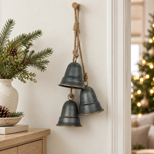 Metal hanging bells on a cream wall beside a console with evergreen Christmas foliage