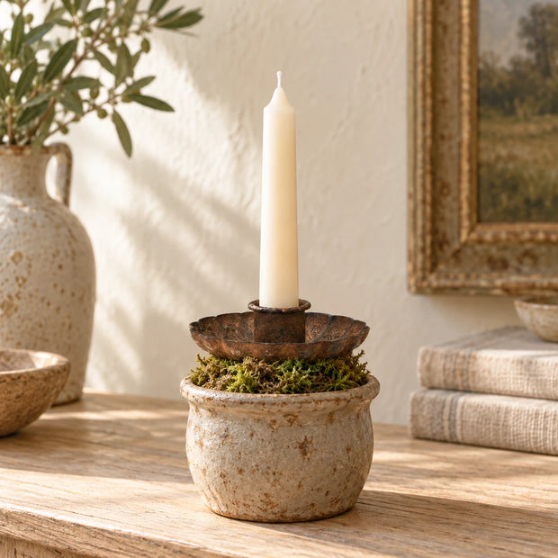 Flat rust candle holder styled with an ivory taper in a small moss-filled pot
