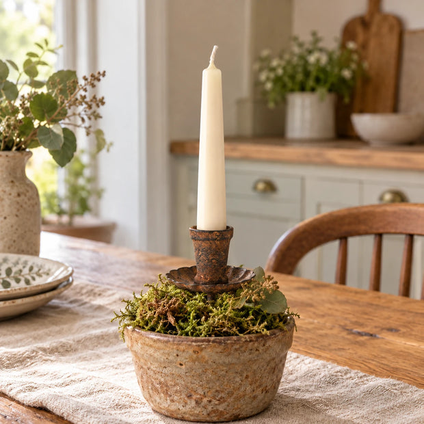 Tall rust candle holder with an ivory taper on an oak dining table