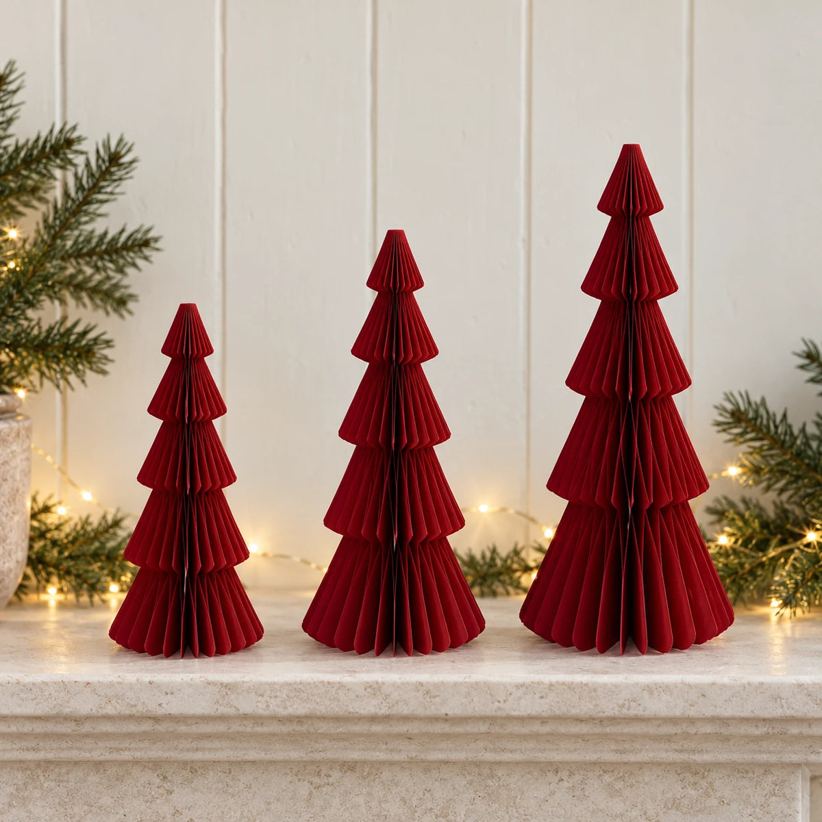 Mixed-size burgundy red standing paper trees side by side on a stone mantel.