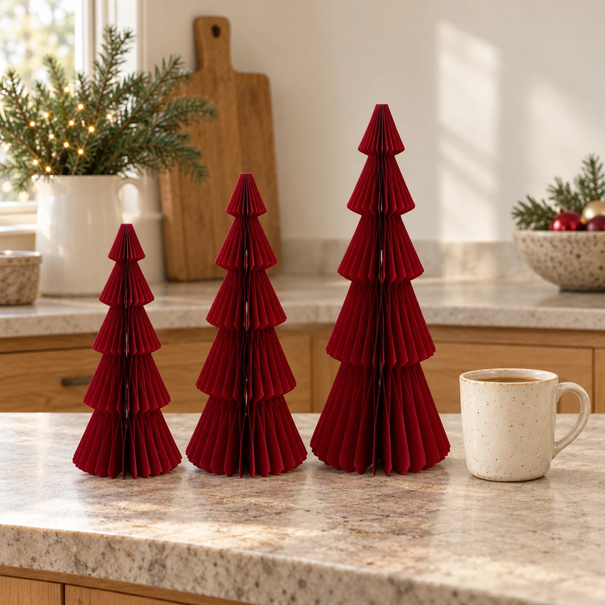burgundy red paper tree set in three heights beside a mug of tea in a country kitchen.