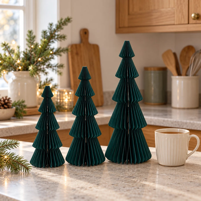 Green paper tree set in three heights beside a mug of tea in a country kitchen.