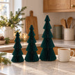 Green paper tree set in three heights beside a mug of tea in a country kitchen.