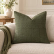 Moss green woven square cushion cover styled on a cream sofa in a neutral living room.