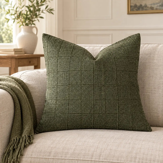 Moss green woven square cushion cover styled on a cream sofa in a neutral living room.