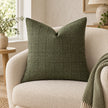 Moss green woven square cushion cover styled on a cream armchair with a green patterned throw.