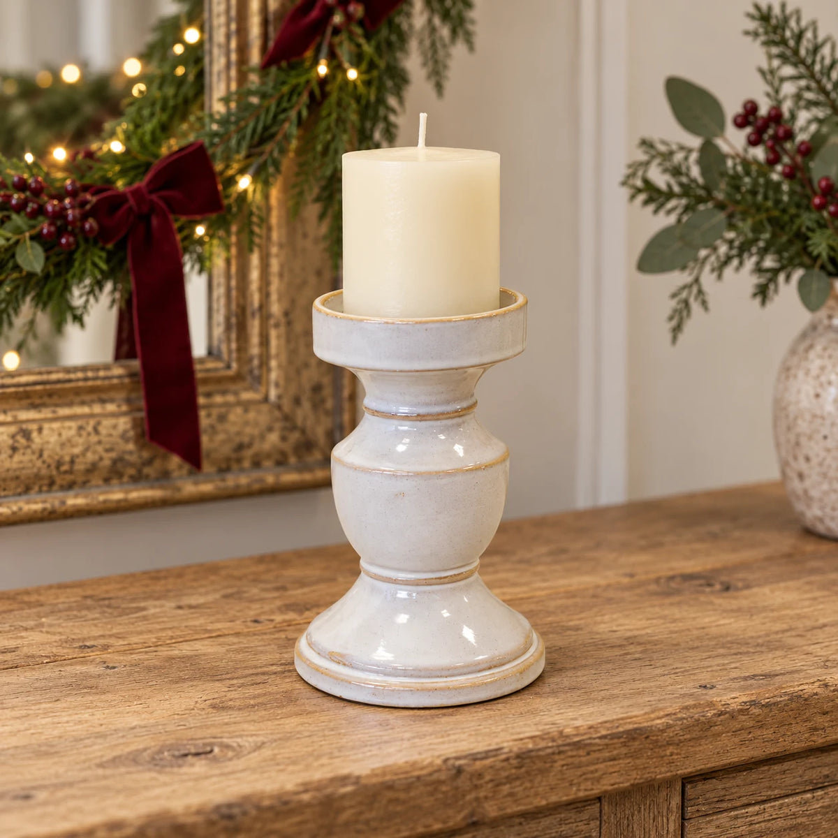 Natural ceramic candle holder with an ivory pillar candle on a Christmas console