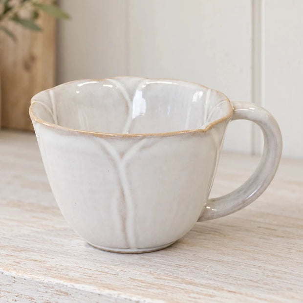 Natural ceramic cup with flower-petal detailing on a whitewashed kitchen shelf