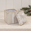 Open natural ceramic gift box with removable bow lid beside evergreen foliage