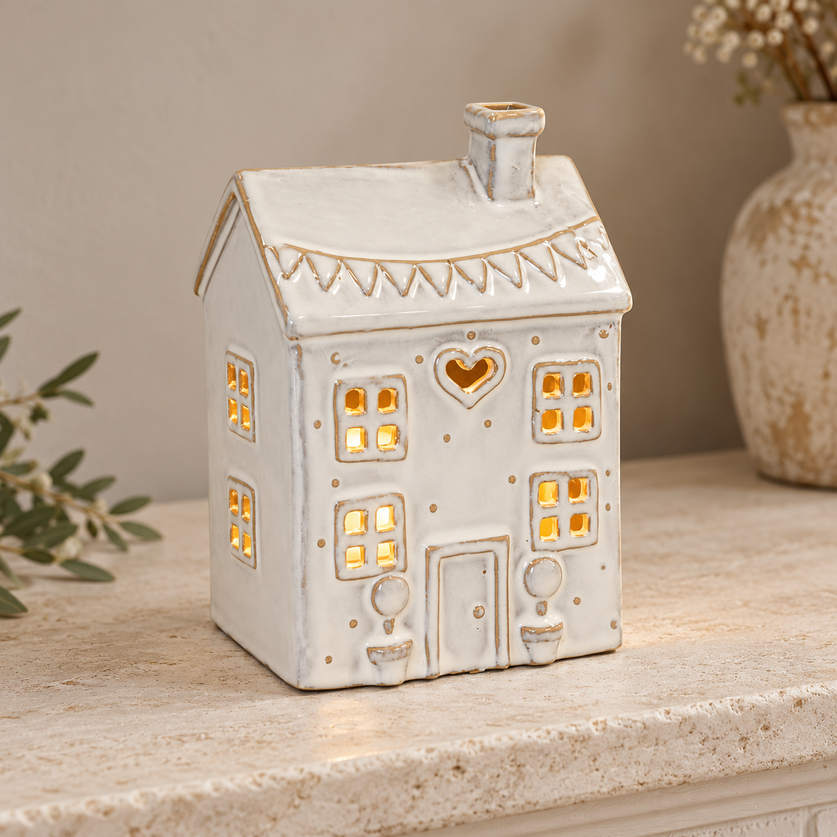 Cream ceramic heart house tealight holder illuminated on a pale stone mantel