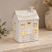 Cream ceramic heart house tealight holder illuminated on a pale stone mantel