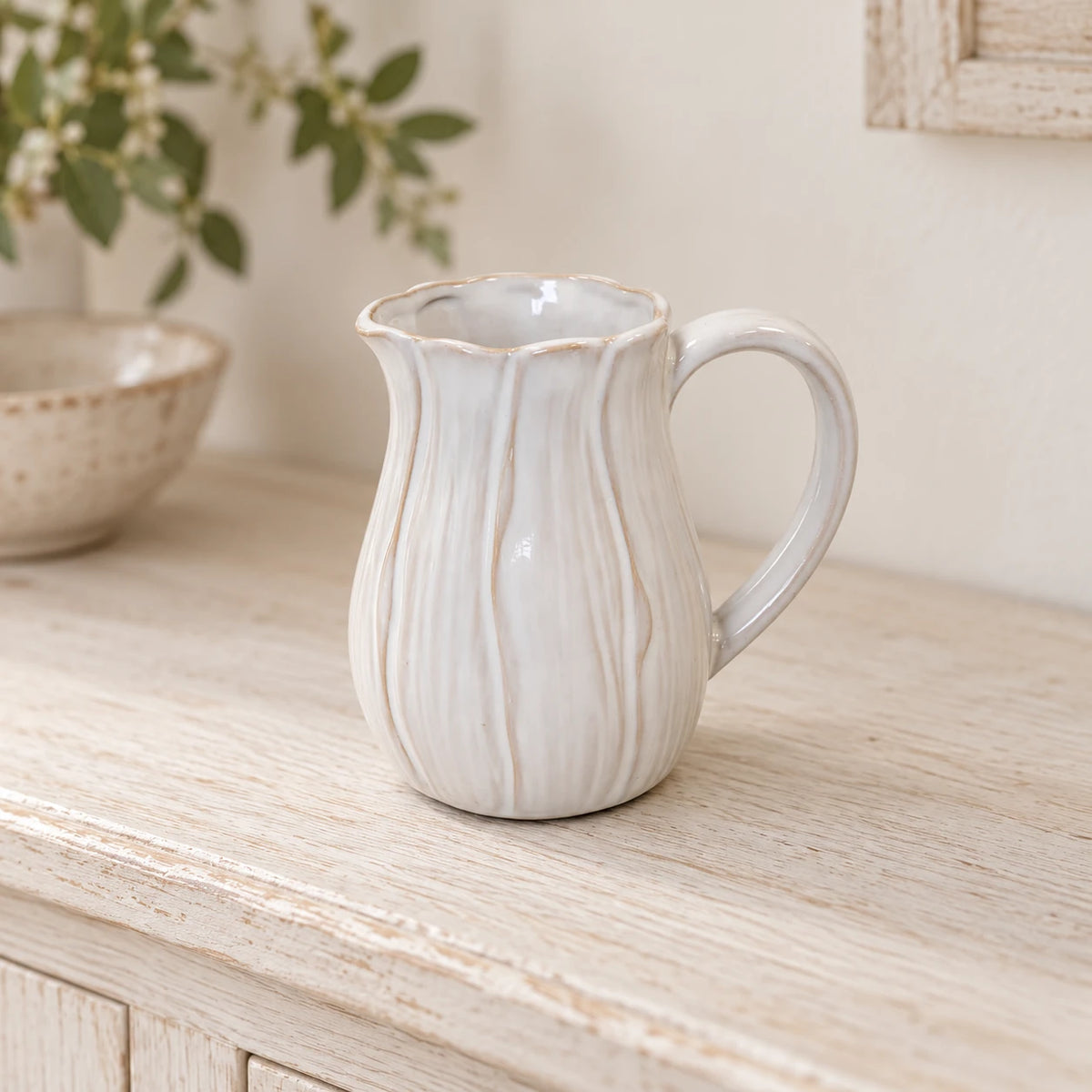 Small natural ceramic jug with petal-shaped detailing on a whitewashed oak shelf