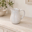 Small natural ceramic jug with petal-shaped detailing on a whitewashed oak shelf