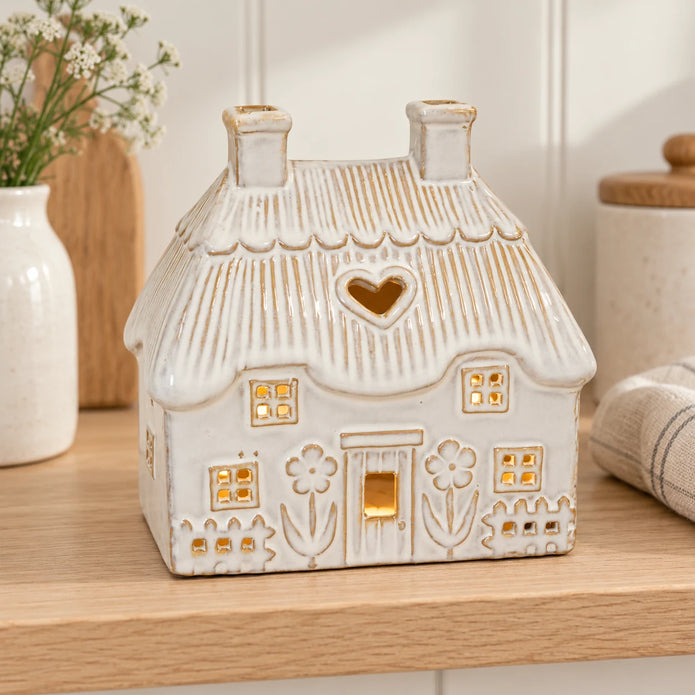 Natural ivory ceramic thatch roof tealight house, 16cm wide, shelf view, styled with a gentle LED tealight glow.