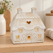 Natural ivory ceramic thatch roof tealight house, 16cm wide, shelf view, styled with a gentle LED tealight glow.