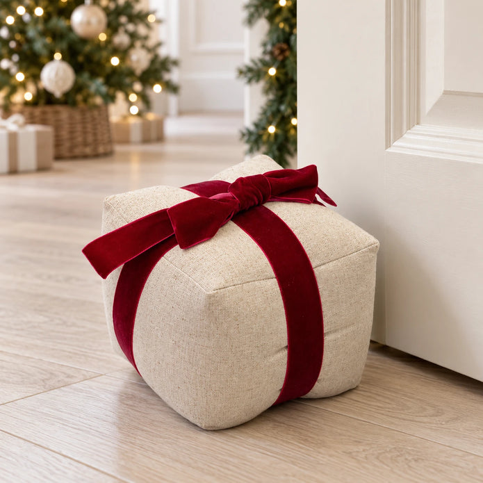 Natural linen present doorstop with red velvet bow beside a cream door at Christmas