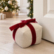 Natural linen present doorstop with red velvet bow beside a cream door at Christmas