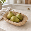 Natural pine mini dough bowl holding three green pears on a cream kitchen counter beside linen.