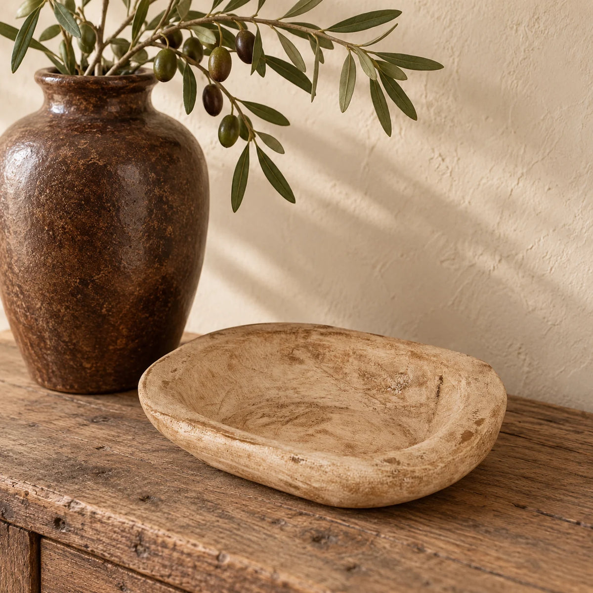 Pale natural pine mini dough bowl styled empty on an oak console beside a tall brown ceramic vase.