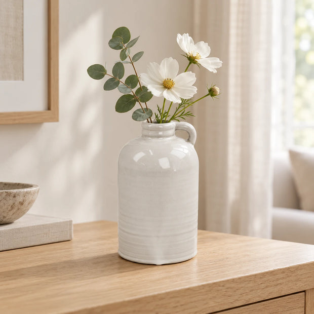 Natural stoneglazed short jug vase with white flowers and eucalyptus on a pale wood console