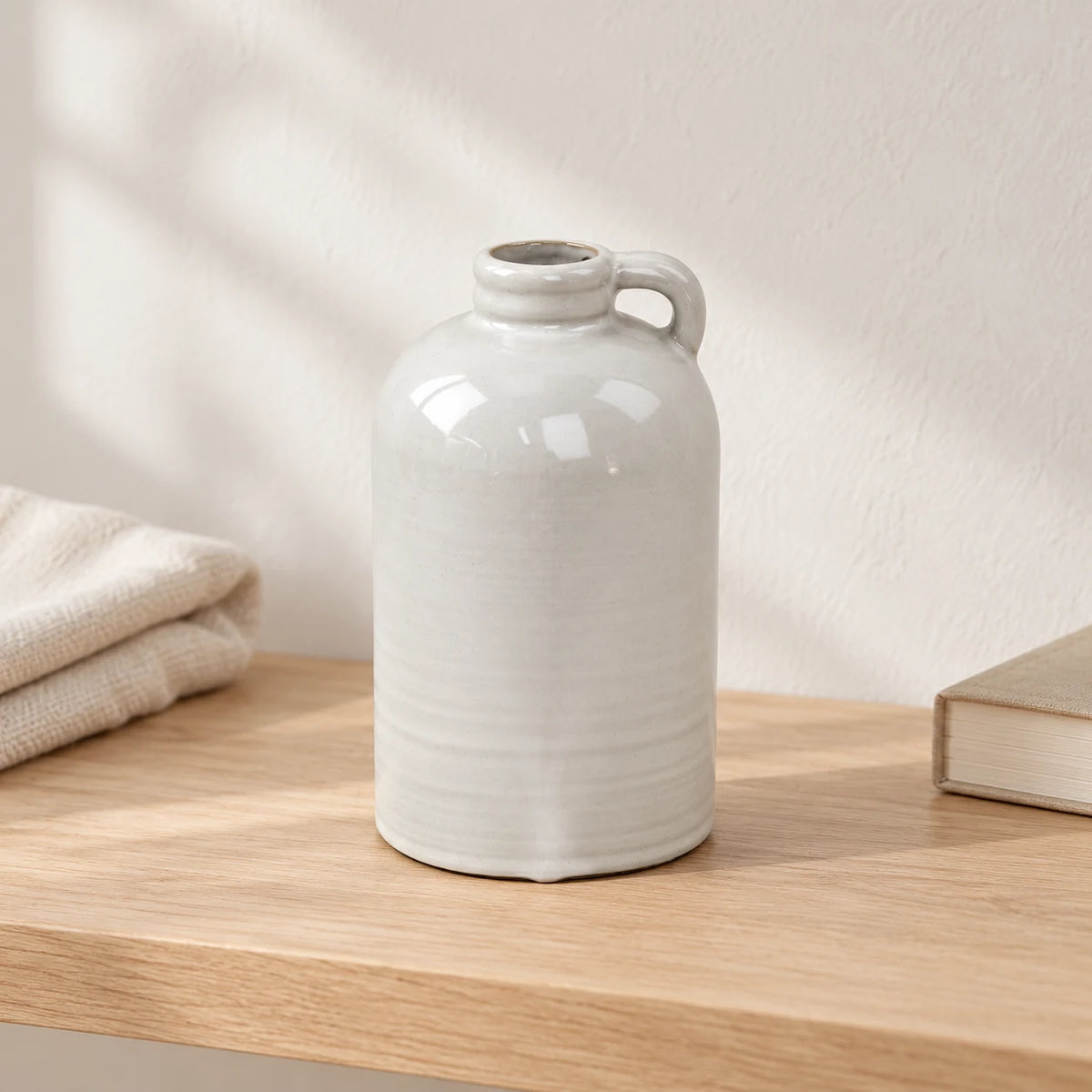 Natural stoneglazed short jug vase displayed empty on a pale wood shelf