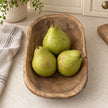 Natural walnut mini dough bowl holding three pears on a cream kitchen worktop beside oatmeal linen.