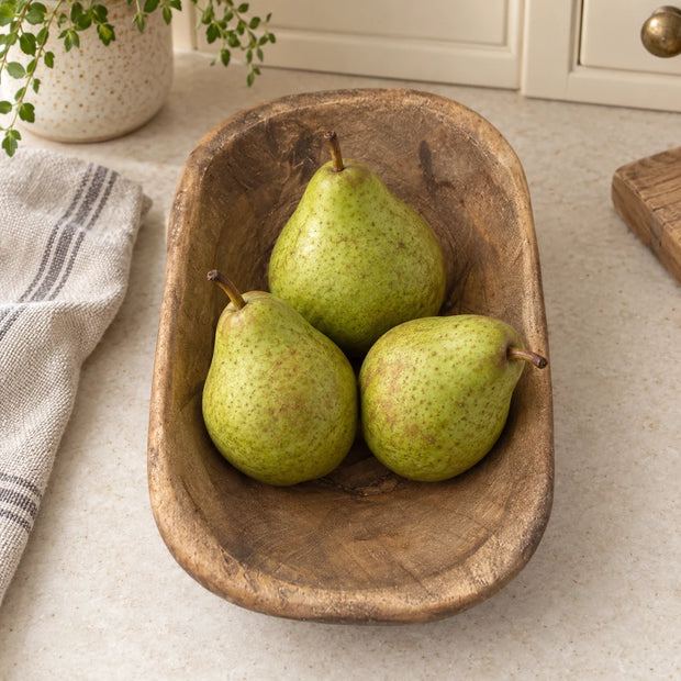 Natural walnut mini dough bowl holding three pears on a cream kitchen worktop beside oatmeal linen.