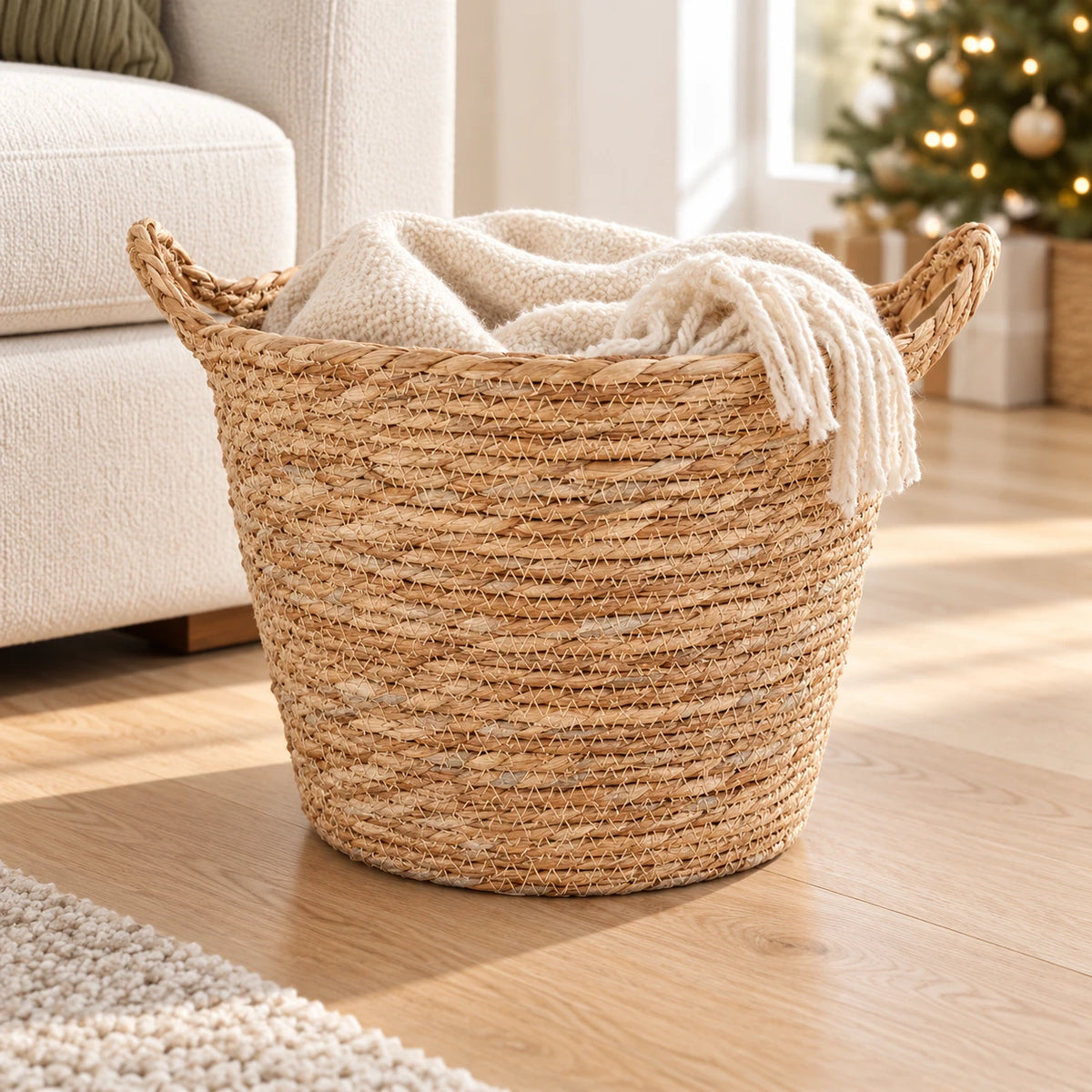 Natural woven basket with two handles holding a cream throw beside a sofa in a Christmas living room