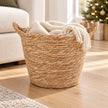 Natural woven basket with two handles holding a cream throw beside a sofa in a Christmas living room