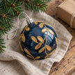 Navy blue and gold Christmas bauble by Starlight Express hanging on a decorated holiday tree with lights and ornaments.