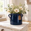 Navy blue milk churn pot styled with cream flowers beside a cottage window