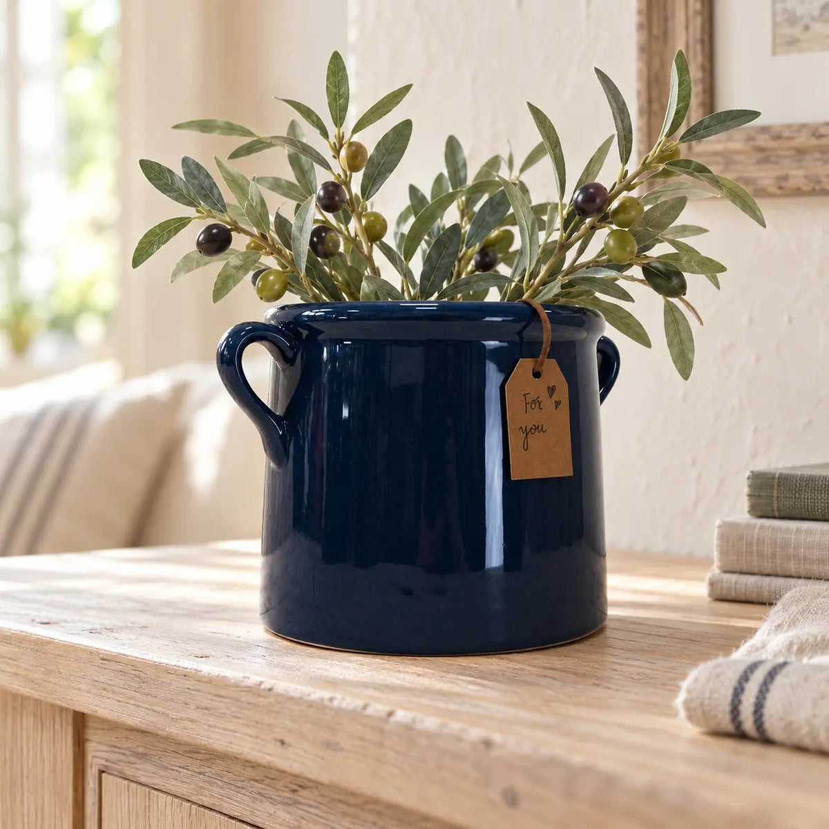Navy blue milk churn stoneware pot with olive sprigs on a pale oak console