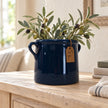 Navy blue milk churn stoneware pot with olive sprigs on a pale oak console